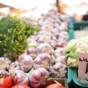 Colorful array of garlic, tomatoes, and cauliflower at an outdoor market stall.
