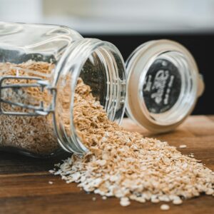 Oats spilling from a glass jar on a wooden surface creating a rustic kitchen scene.